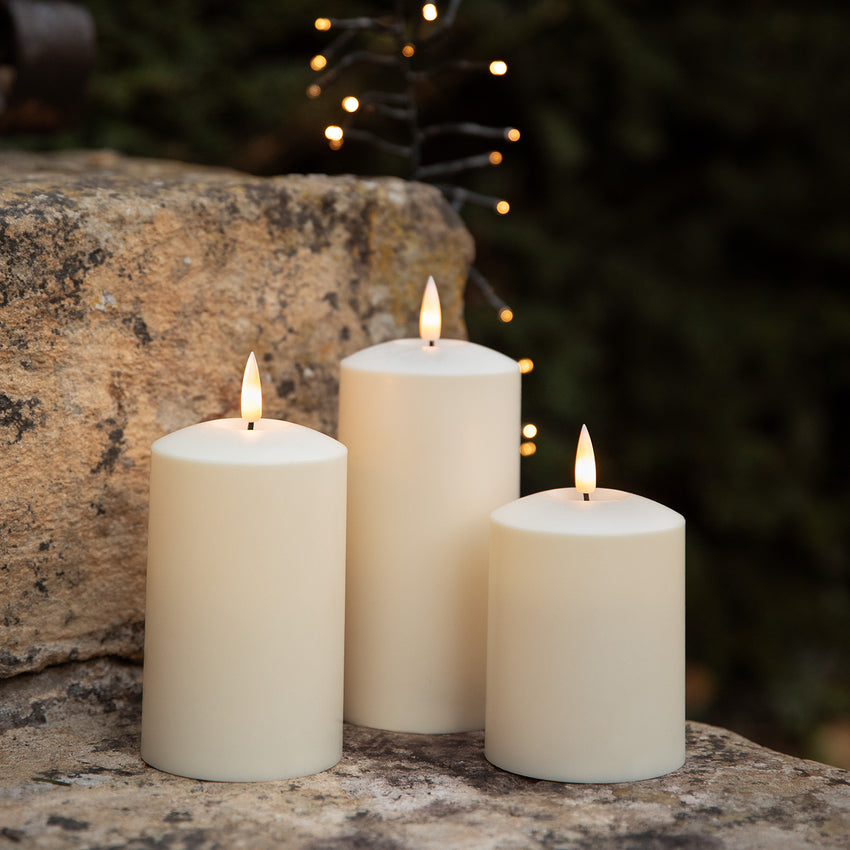 Drei cremefarbene Solar-Kerzen auf einer Steinmauer mit warm leuchtender Lichterkette im Hintergrund.
