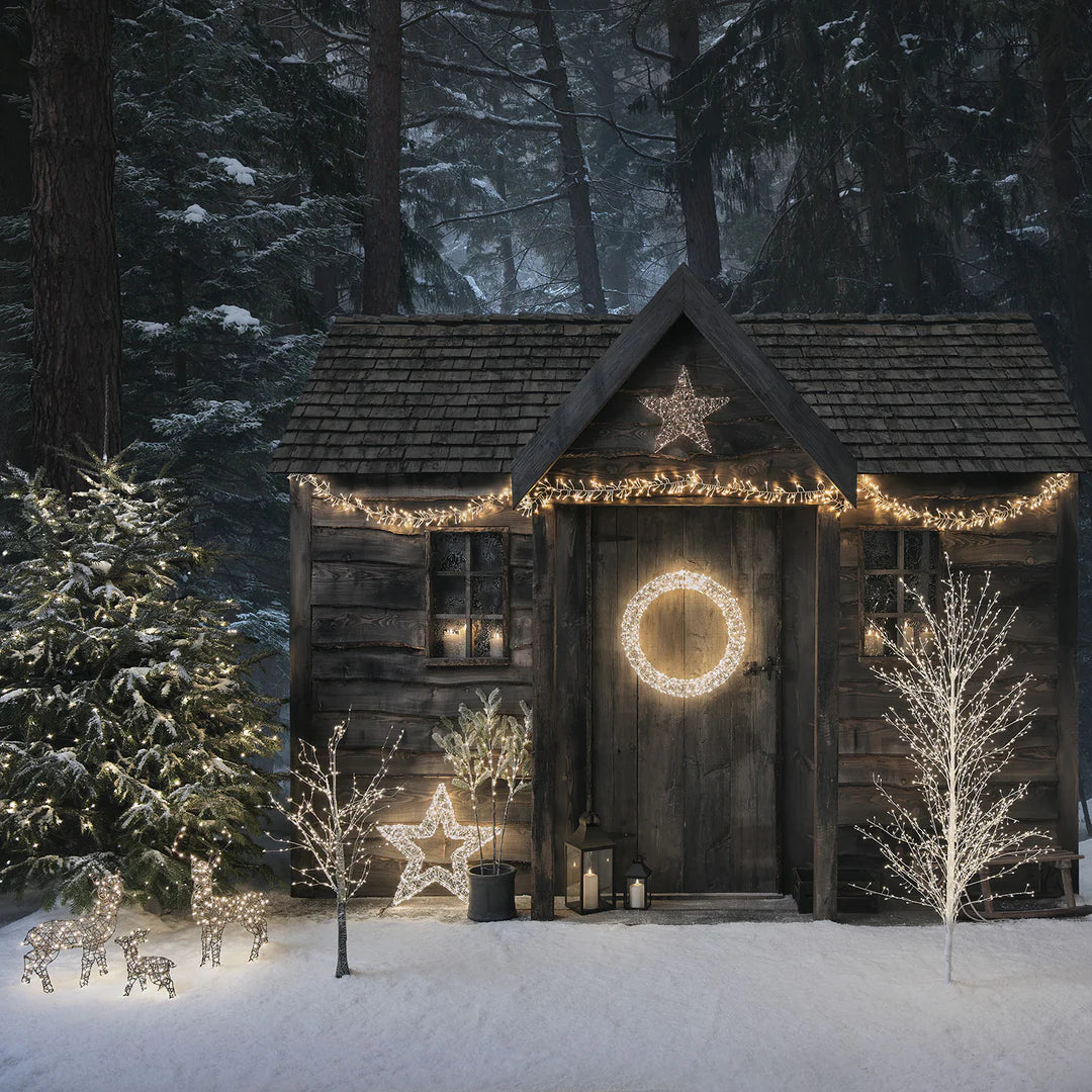 Winterliche Hütte mit beleuchtetem LED-Kranz an Tür, Lichterketten und Deko im Schnee