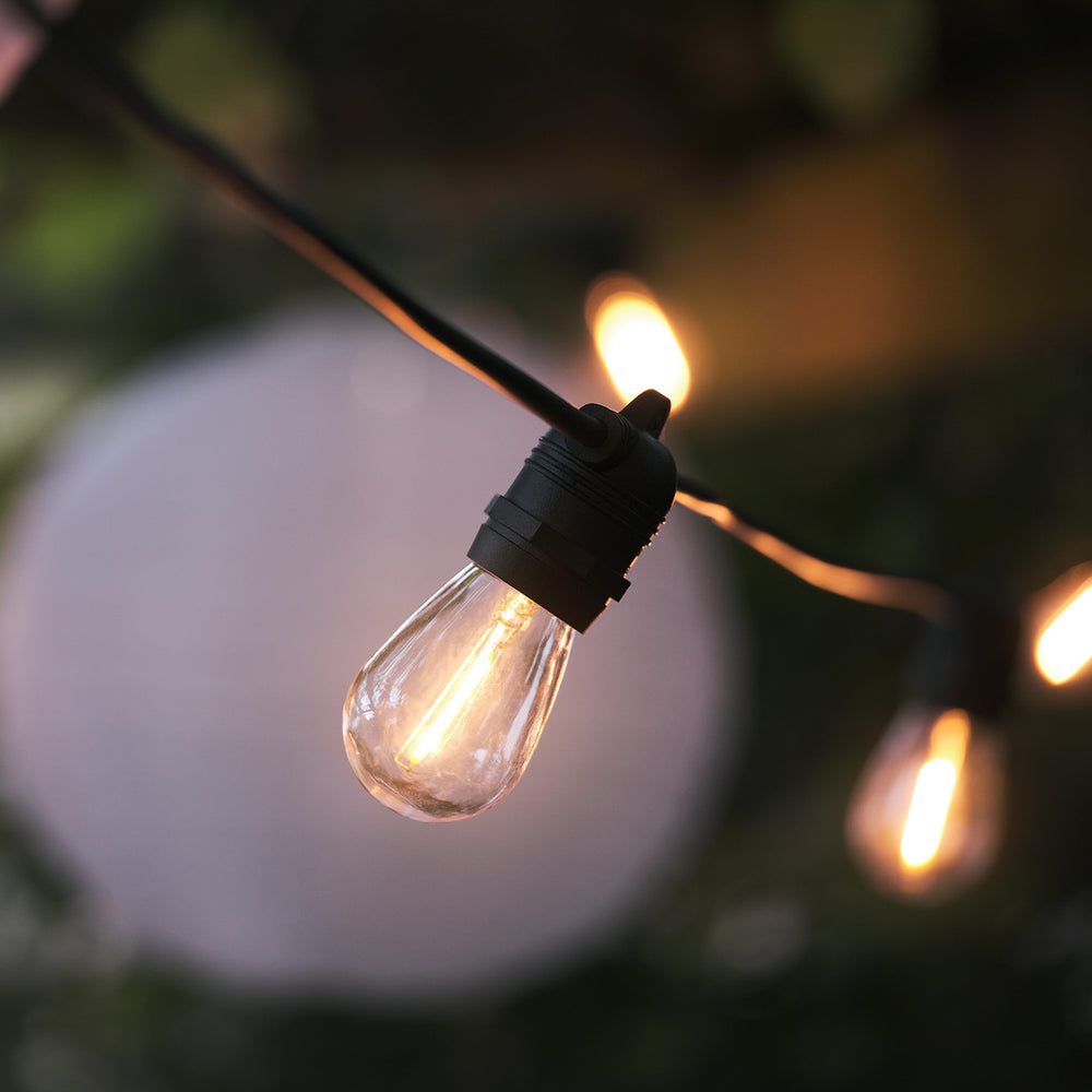 Nahaufnahme einer warmweißen LED-Glühbirne an schwarzem Kabel, unscharfer Hintergrund