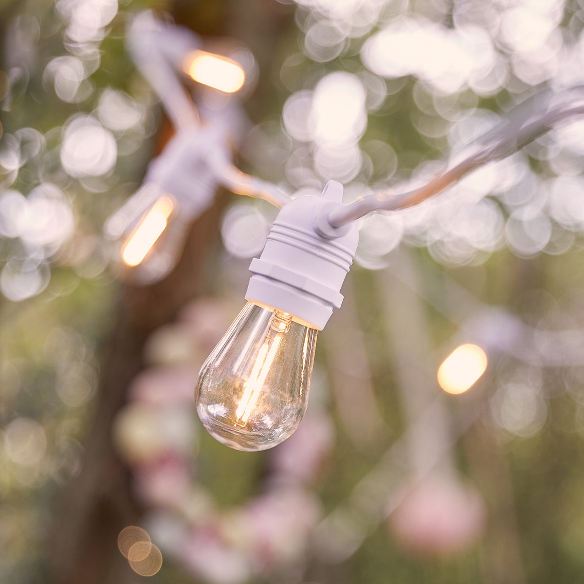 Nahaufnahme einer warmweißen LED-Glühbirne an weißem Kabel mit unscharfem Hintergrund