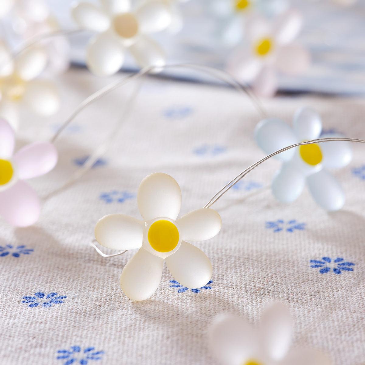 Nahaufnahme einer LED-Lichterkette mit weißen Gänseblümchen auf Stoff mit blauen Blumenmuster