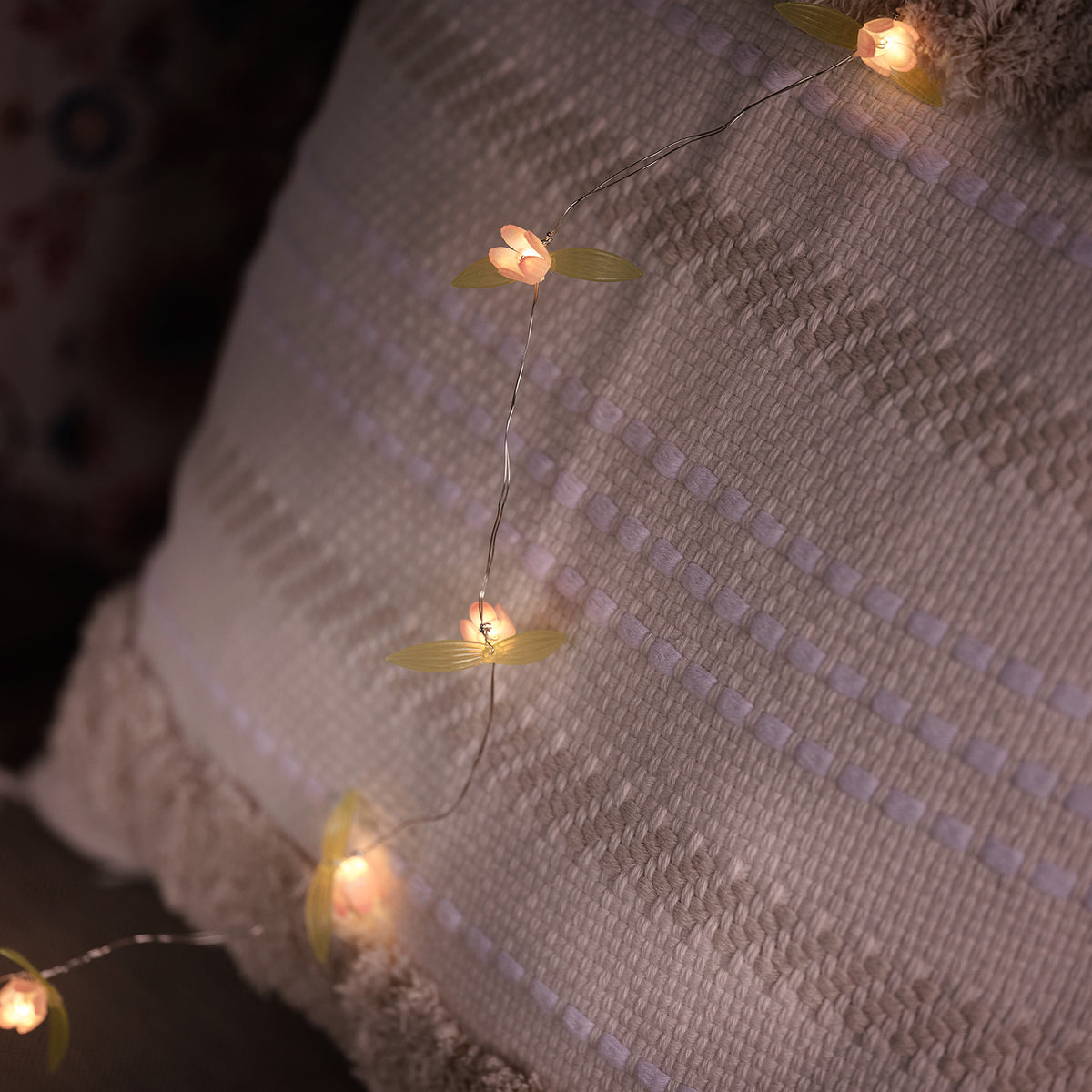 LED-Lichterkette mit gelben Blüten auf cremefarbenem Kissen mit Strukturmuster