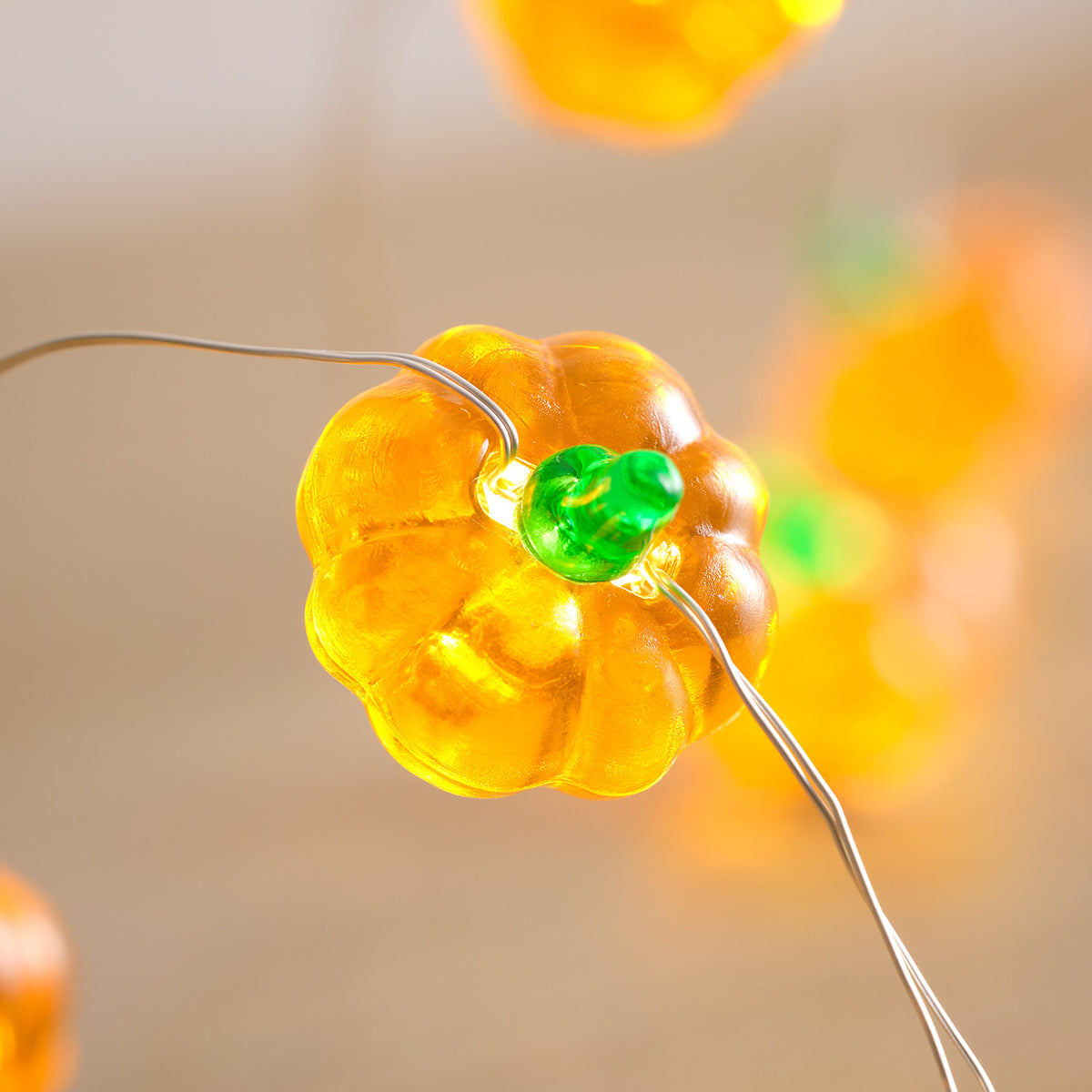Detailaufnahme einer orangefarbenen Kürbis-LED mit grünem Stiel an Lichterkette