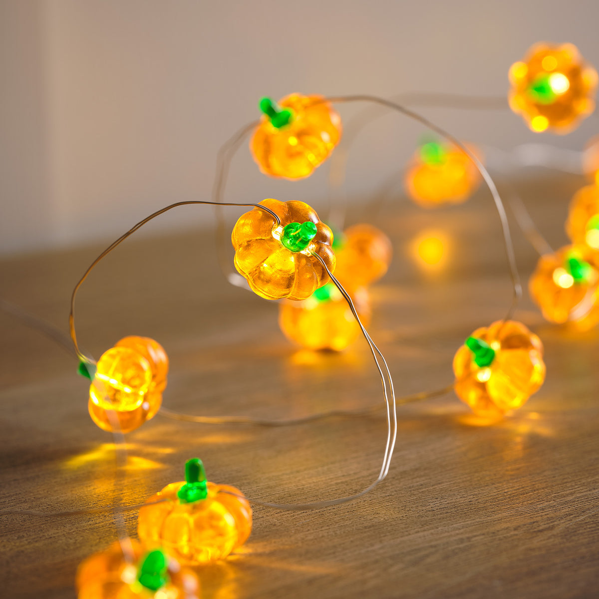 Mehrere leuchtende Kürbis-LEDs an dünnem Kabel auf hellem Untergrund