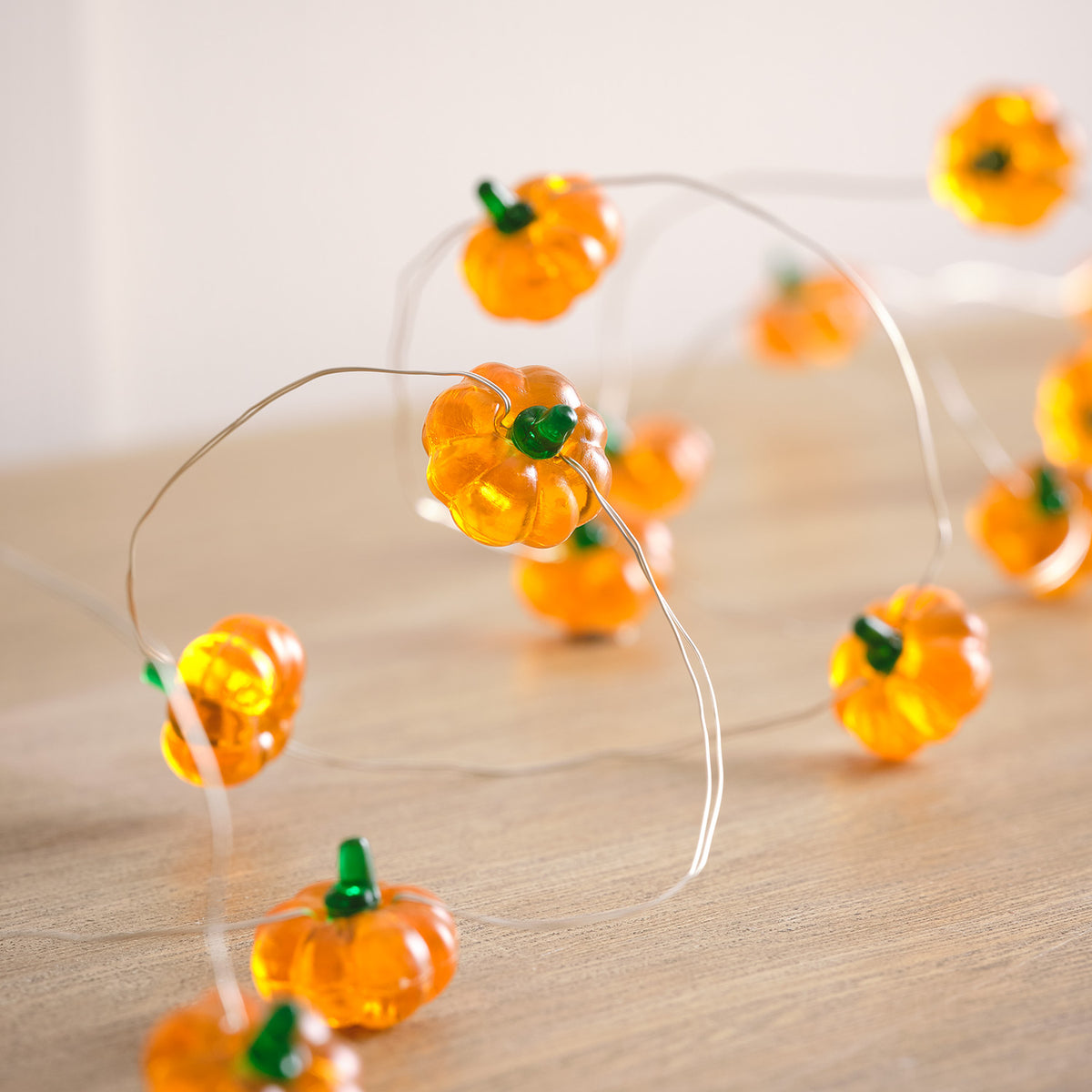 Kürbis-LEDs an Lichterkette auf hellem Holztisch aus nächster Nähe