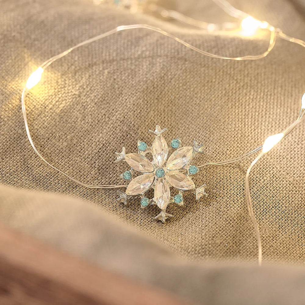Kristall-Schneeflocken-LED-Lichterkette mit funkelnden Edelstein-Anhängern auf beigefarbenem Stoff, warmweiße LED-Lichter mit bokeh Hintergrund.
