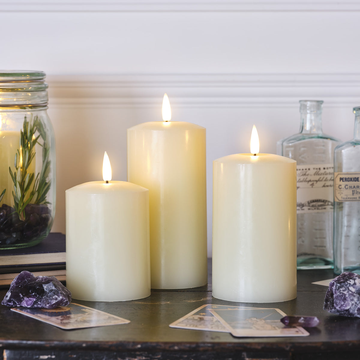 LED Echtwachskerzen auf einem weißen Hocker mit getrockneten Blumen und Lichterkette