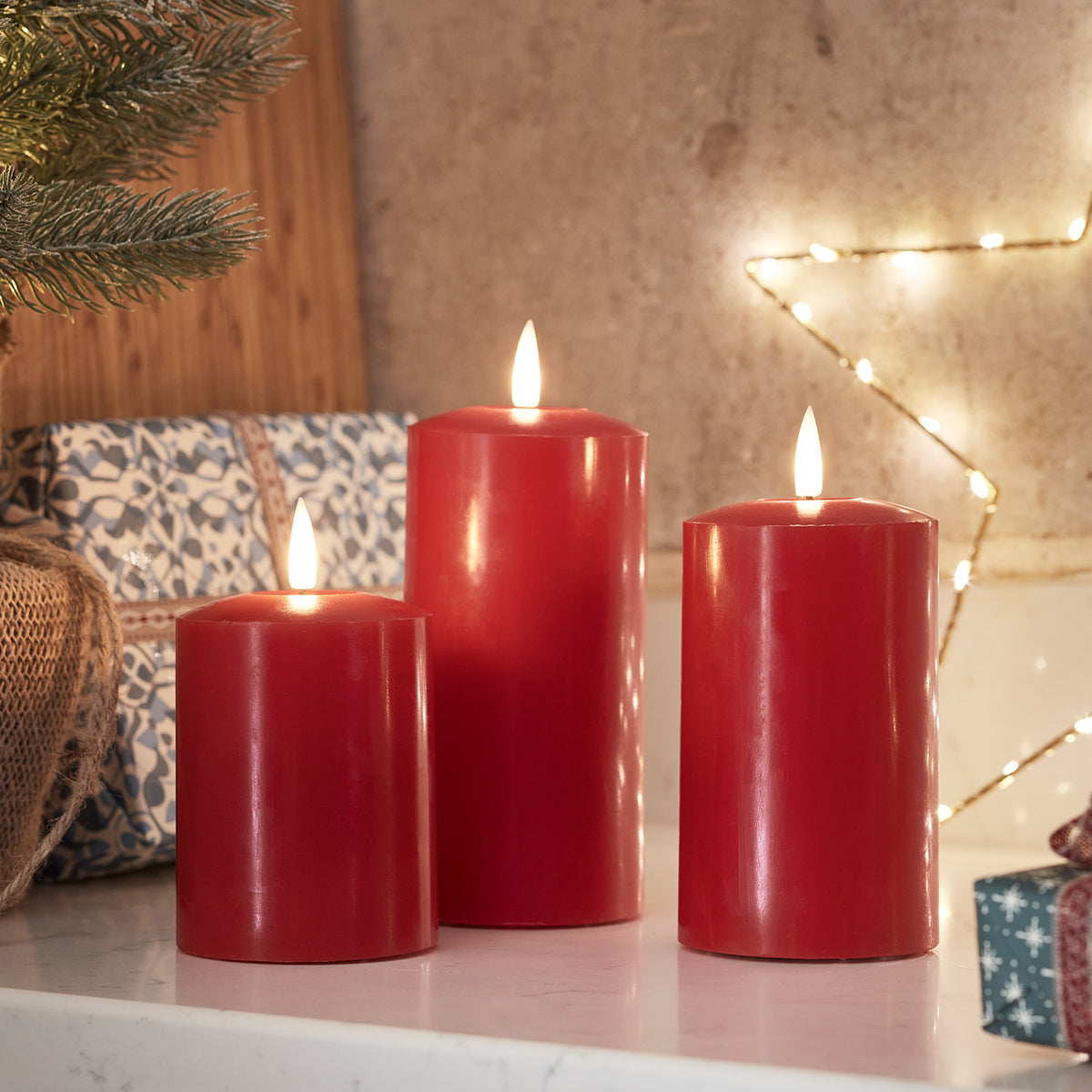 Rotes LED-Kerzen-Trio aus Echtwachs auf weißer Oberfläche mit weihnachtlicher Dekoration