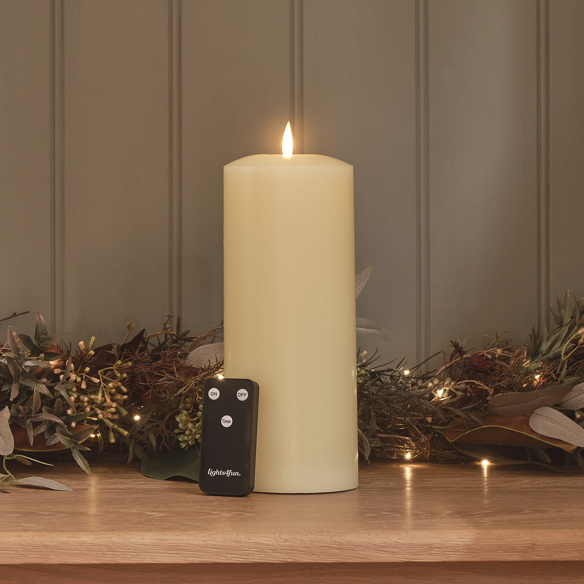 TruGlow LED Stumpenkerze mit schwarzer Fernbedienung auf Holzfläche mit Lichtergirlande
