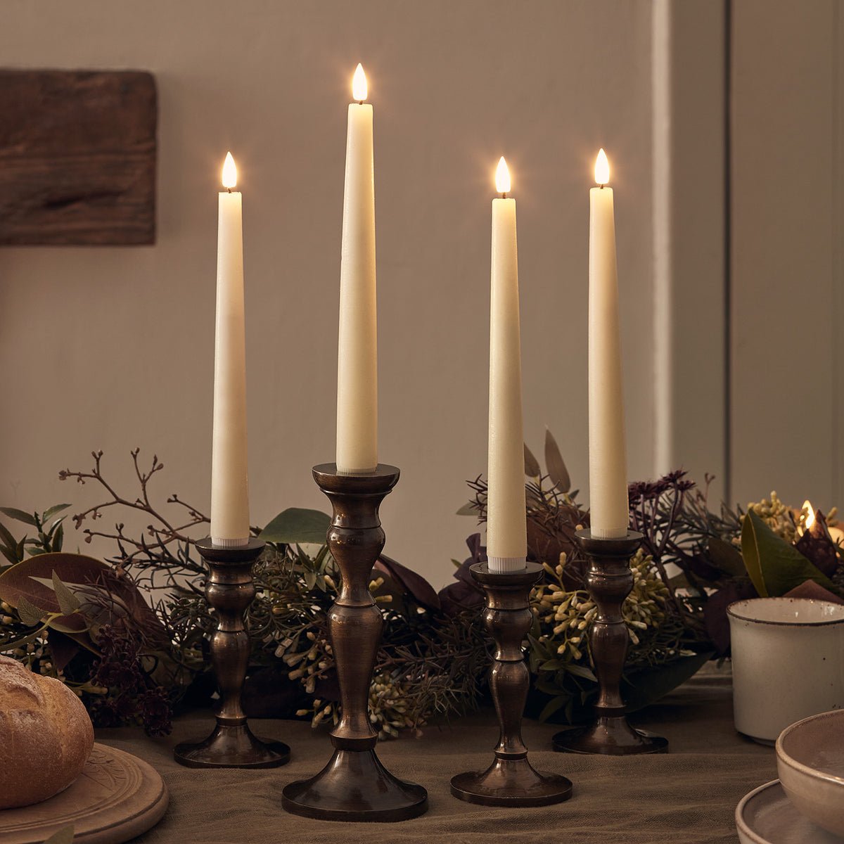 Vier LED Stabkerzen in dunklen Kerzenhaltern auf einem Tisch mit herbstlicher Dekoration