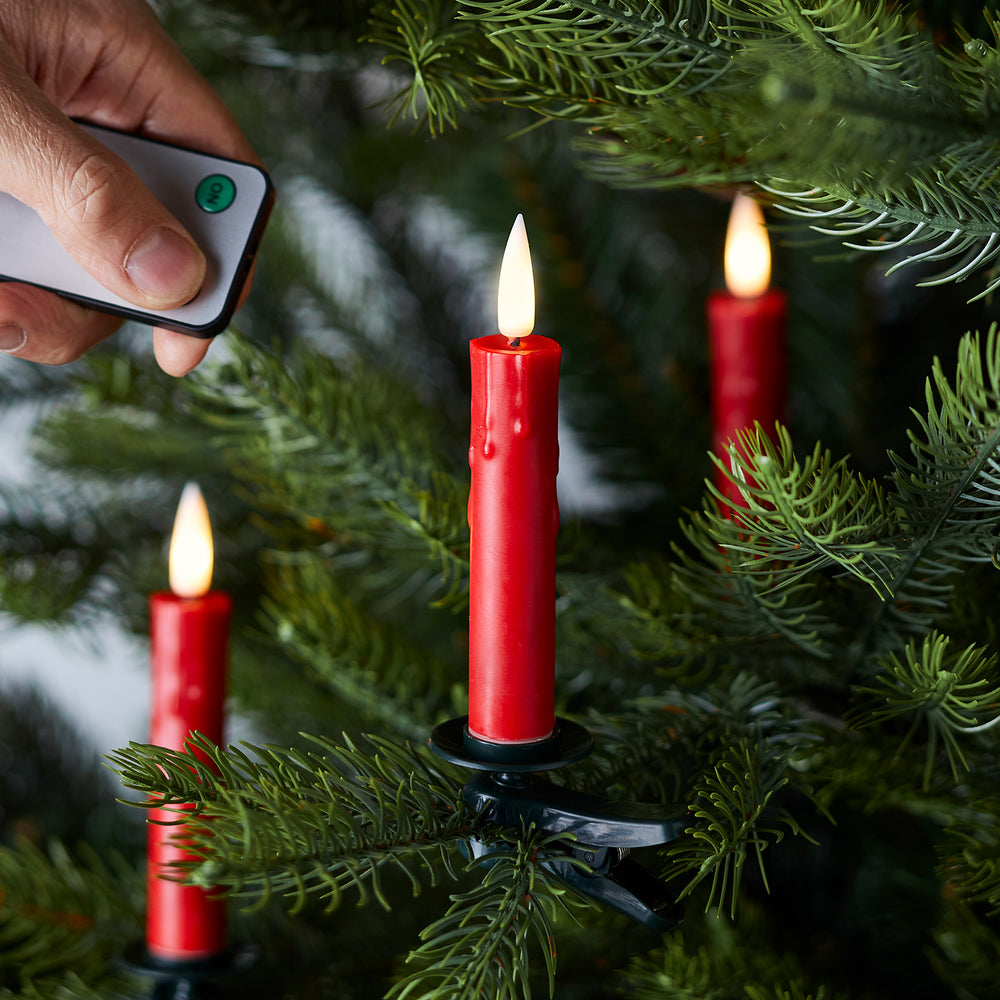 Hand mit Fernbedienung steuert rote LED Baumkerze an Tannenzweig mit Clip