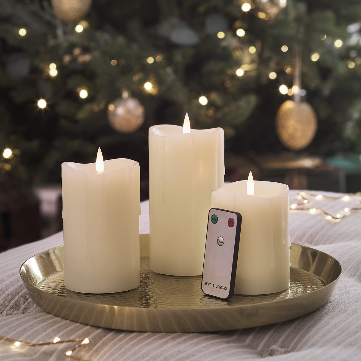 LED Stumpenkerzen mit Fernbedienung auf goldenem Tablett vor weihnachtlicher Dekoration