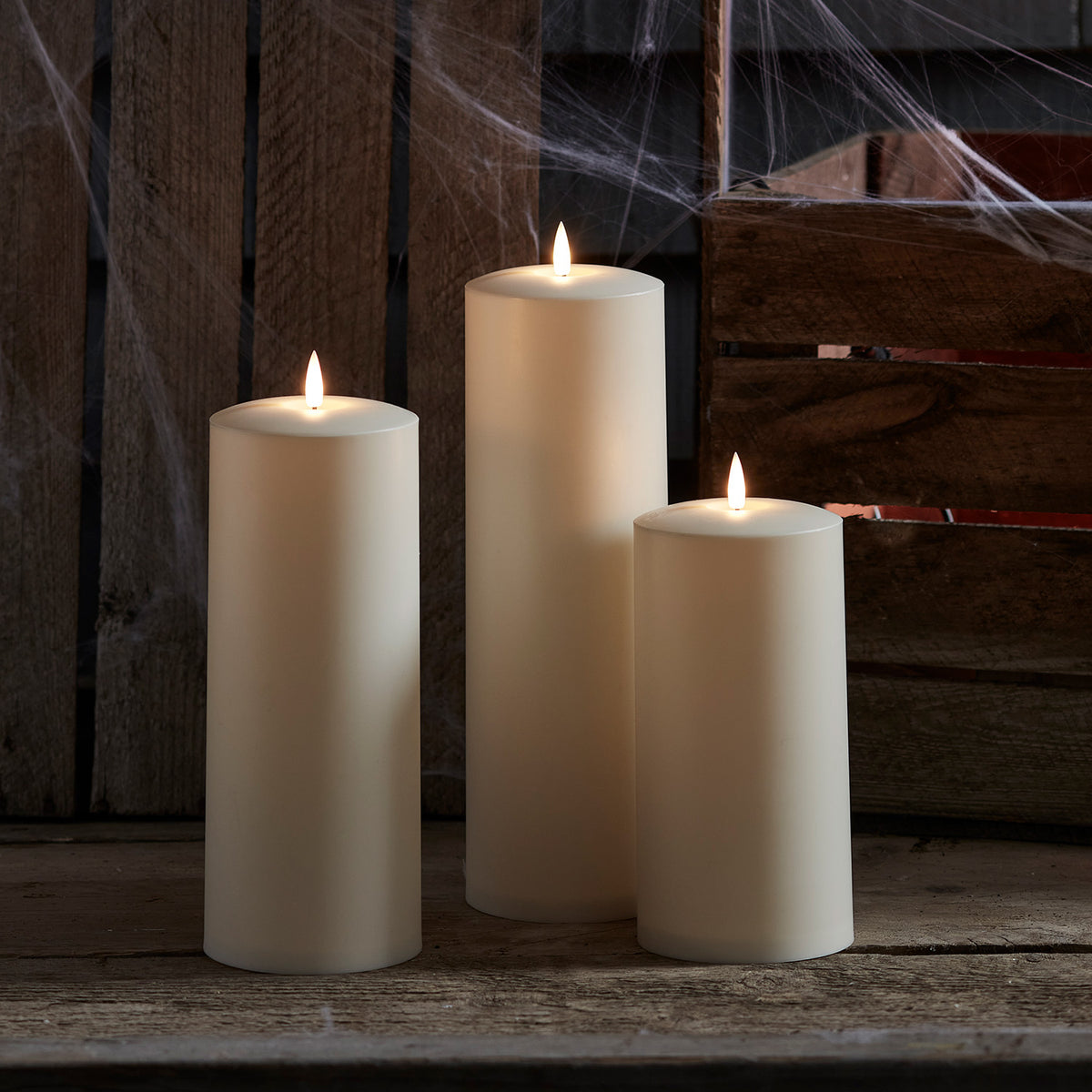 Drei flackernde LED Kerzen vor Holzwand mit Spinnweben in herbstlicher Dekoration
