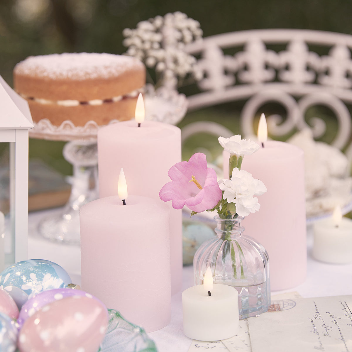 Drei rosa LED-Kerzen in verschiedenen Größen mit Echtwachshülle auf einem Tisch mit Blumen und Osterdeko