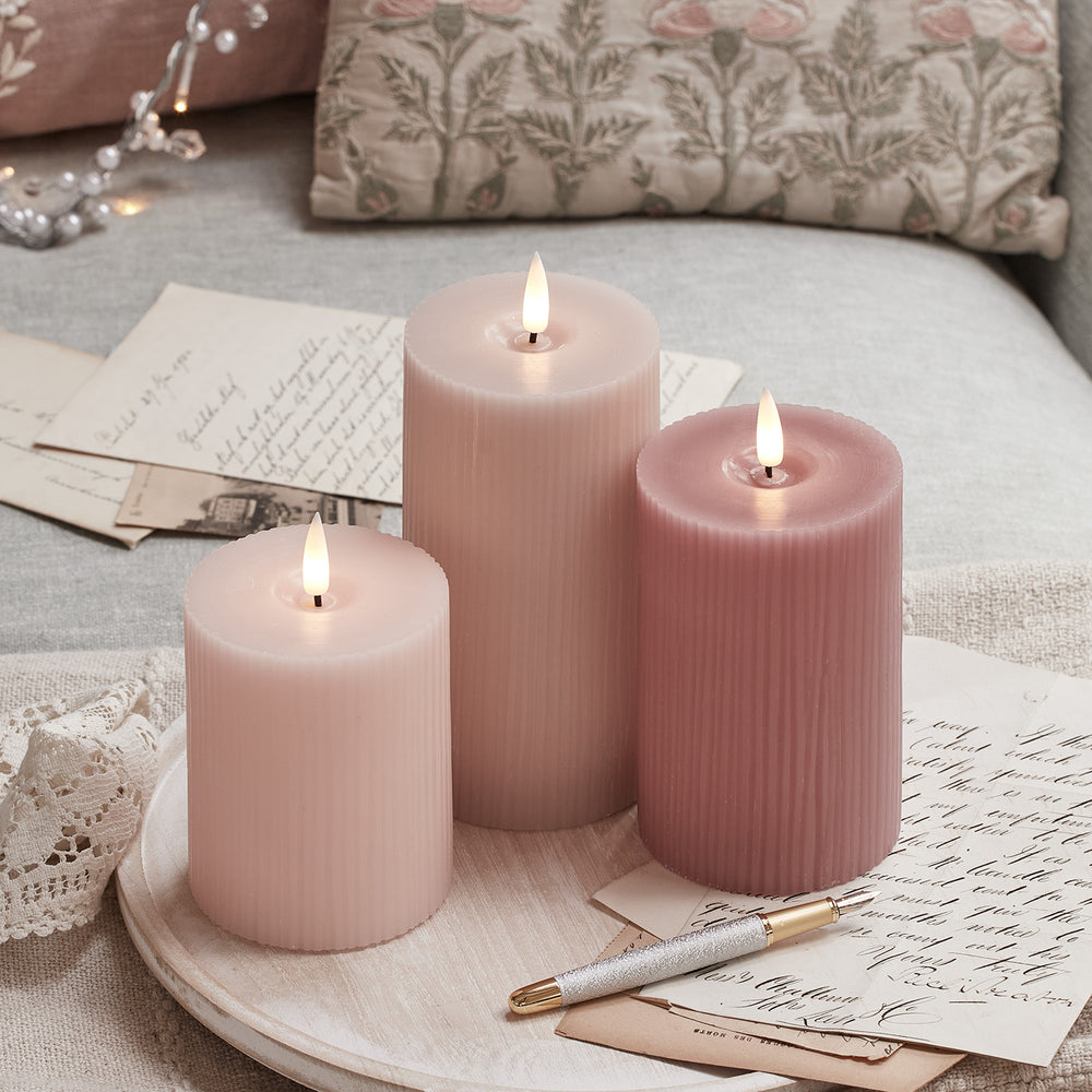 Trio aus geriffelten LED-Kerzen in Rosa- und Pastelltönen auf einem Holztablett mit Briefen