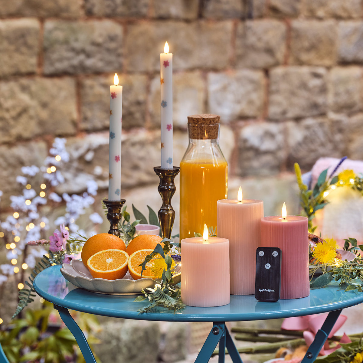 Drei LED-Kerzen in Rosa- und Pastelltönen mit Fernbedienung auf gedecktem Gartentisch