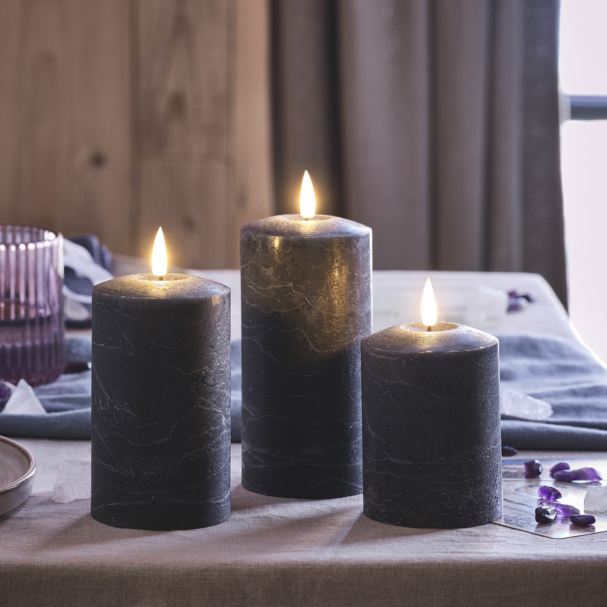 Drei dunkelgraue LED Stumpenkerzen mit flackernden Flammen auf einem Tisch
