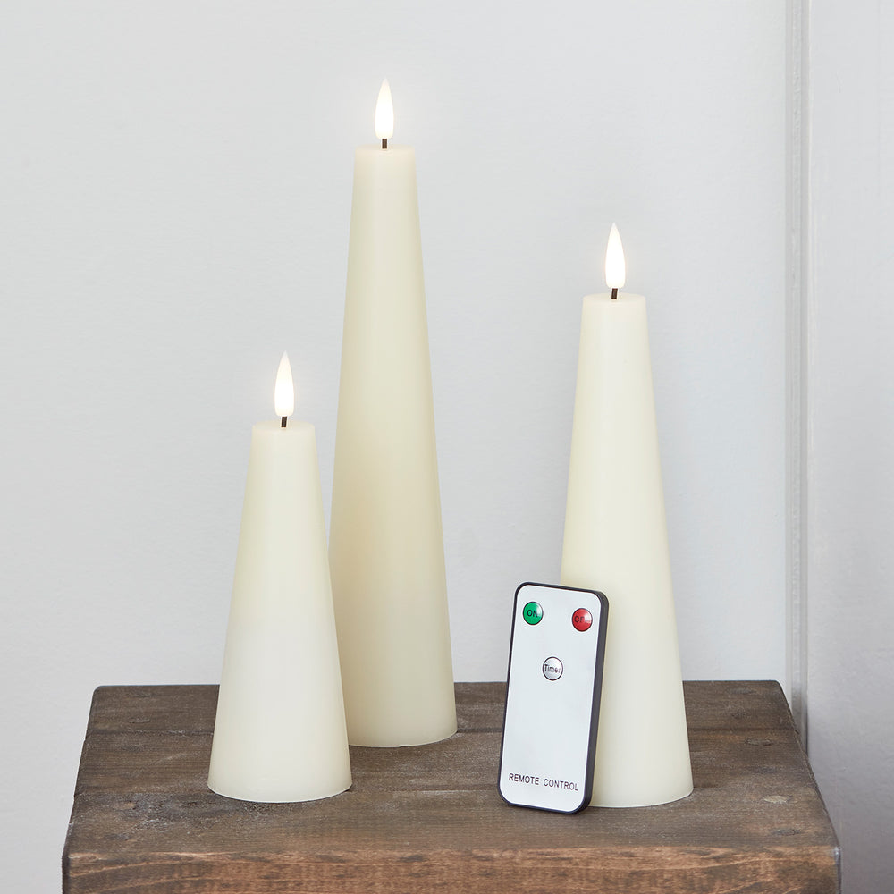 Drei elfenbeinfarbene LED-Kerzen in Kegelform mit Fernbedienung auf Holzuntergrund