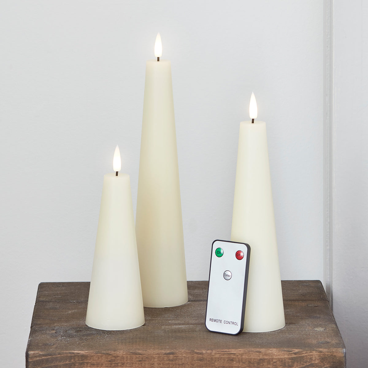 Drei elfenbeinfarbene LED-Kerzen in Kegelform mit Fernbedienung auf Holzuntergrund