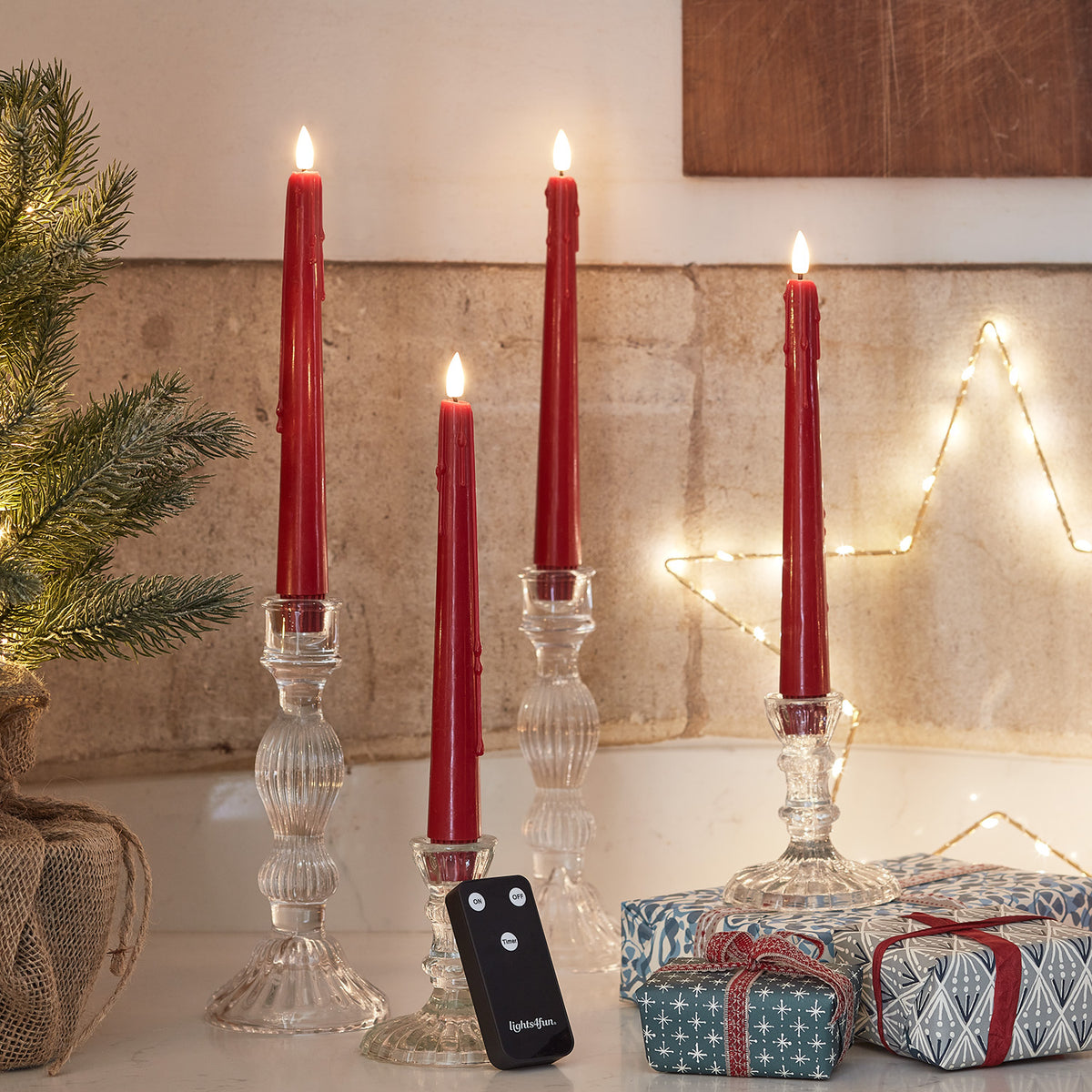 Vier rote LED Stabkerzen mit Wachstropfen und Fernbedienung neben Geschenken und Weihnachtsdeko