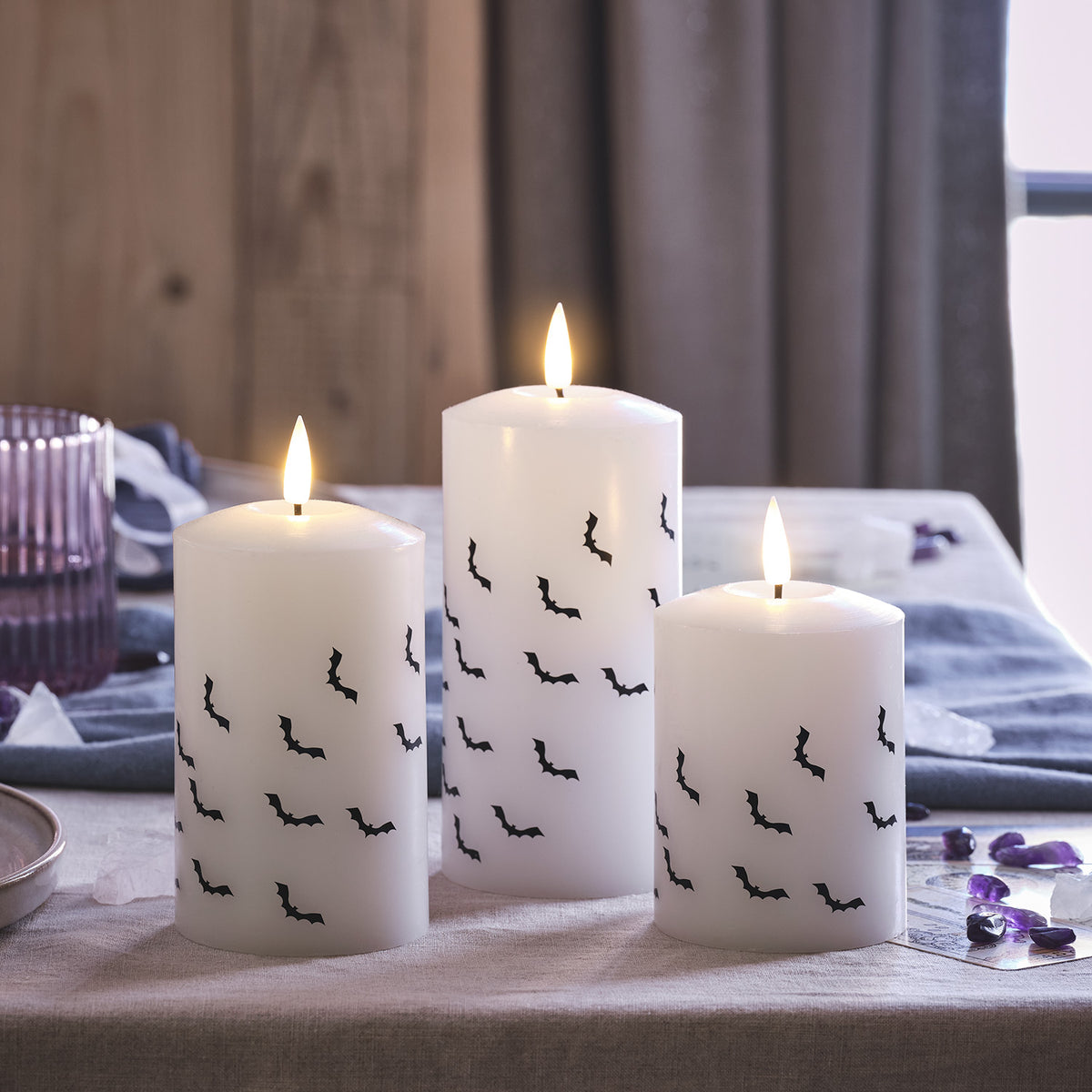 Drei weiße LED Stumpenkerzen mit schwarzen Fledermausmotiven auf einem Tisch