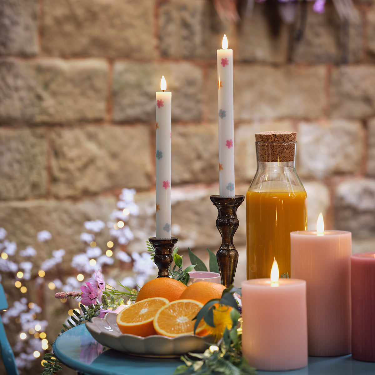LED Stabkerzen mit Blumenmuster in Kerzenhaltern auf blauem Tisch mit Orangen, Kerzen und Saftflasche
