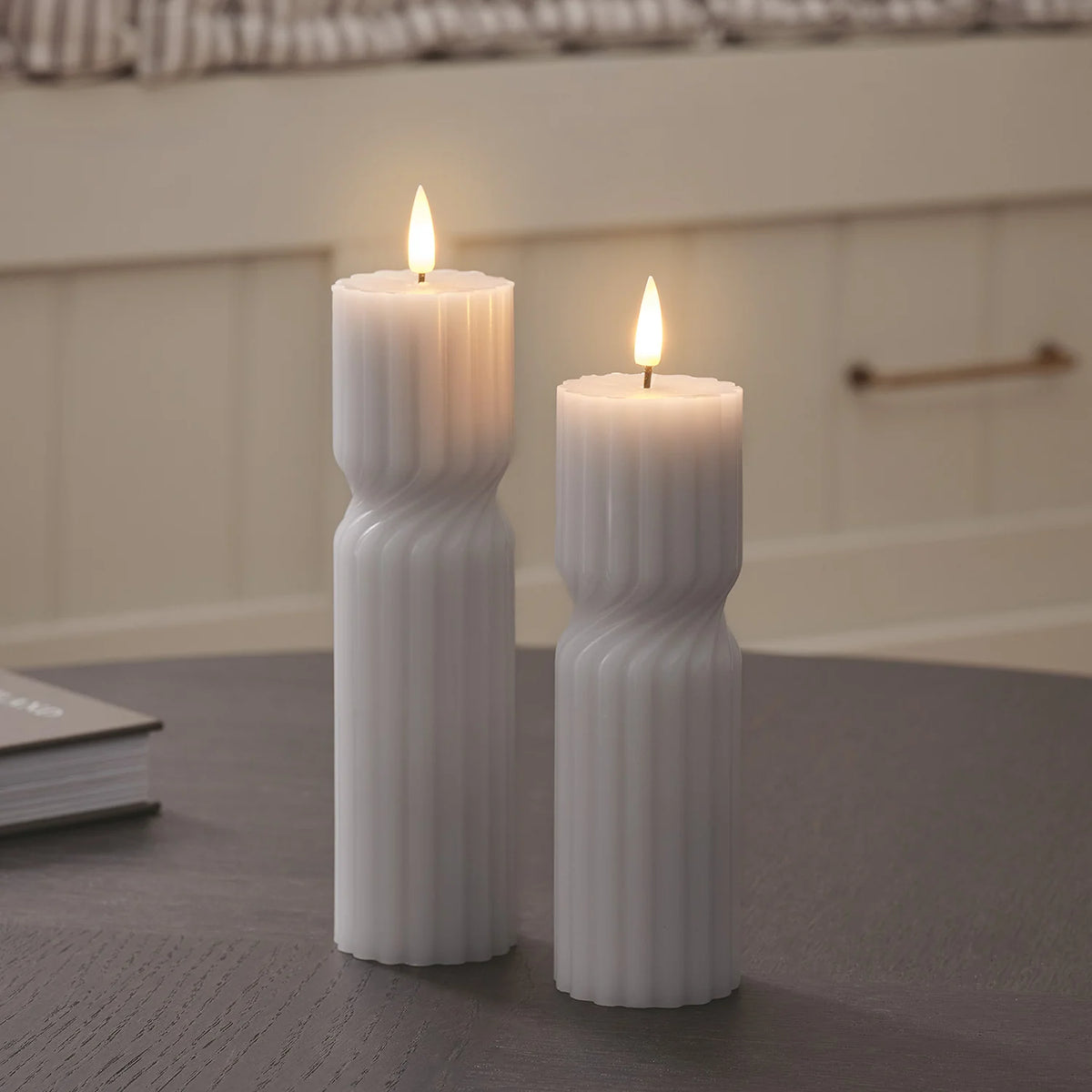 Zwei weiße LED-Stumpenkerzen mit geripptem Twist-Design auf dunklem Tisch