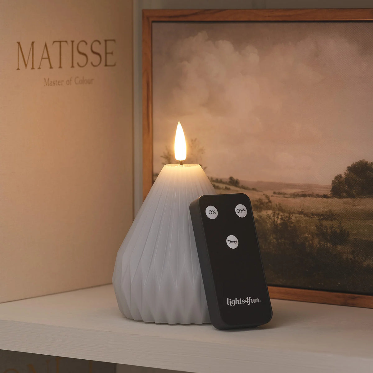 LED-Kerze mit Fernbedienung auf Regal vor Landschaftsbild mit eingeschalteter Flamme