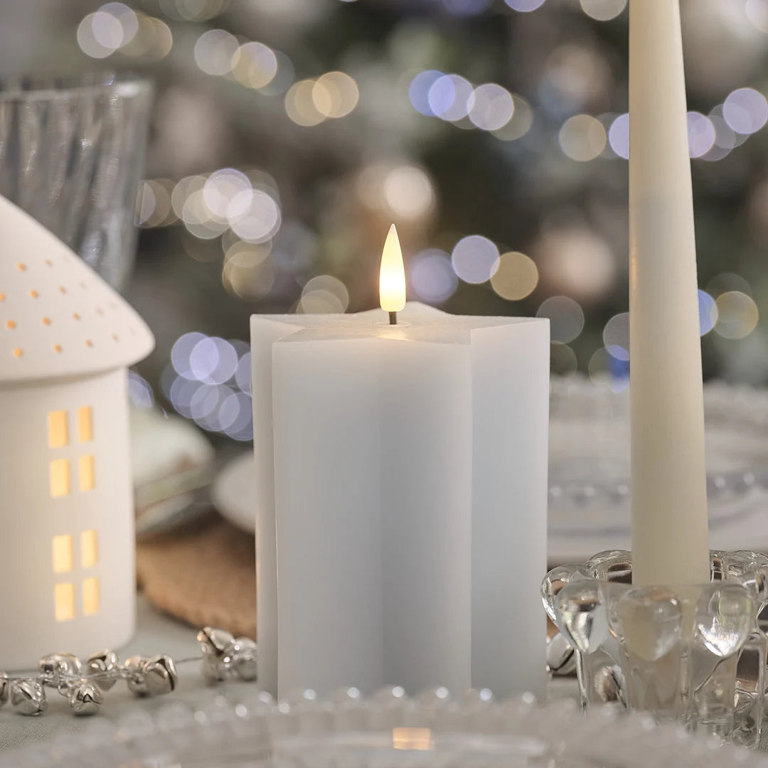 Einzelne weiße LED-Kerze mit realistischer Flamme, Porzellan-Haus mit beleuchteten Fenstern, transparentes Kristallglas-Windlicht, bokeh Weihnachtsbeleuchtung, festliches Styling.