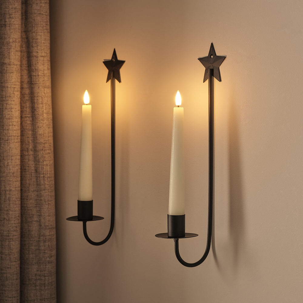 Doppelter wandmontierter LED-Kerzenhalter mit zwei Metallstern-Aufätzen, zwei cremefarbene LED-Kerzen, schwarze Metallkonstruktion mit dekorativer Seiltroschenverbindung.