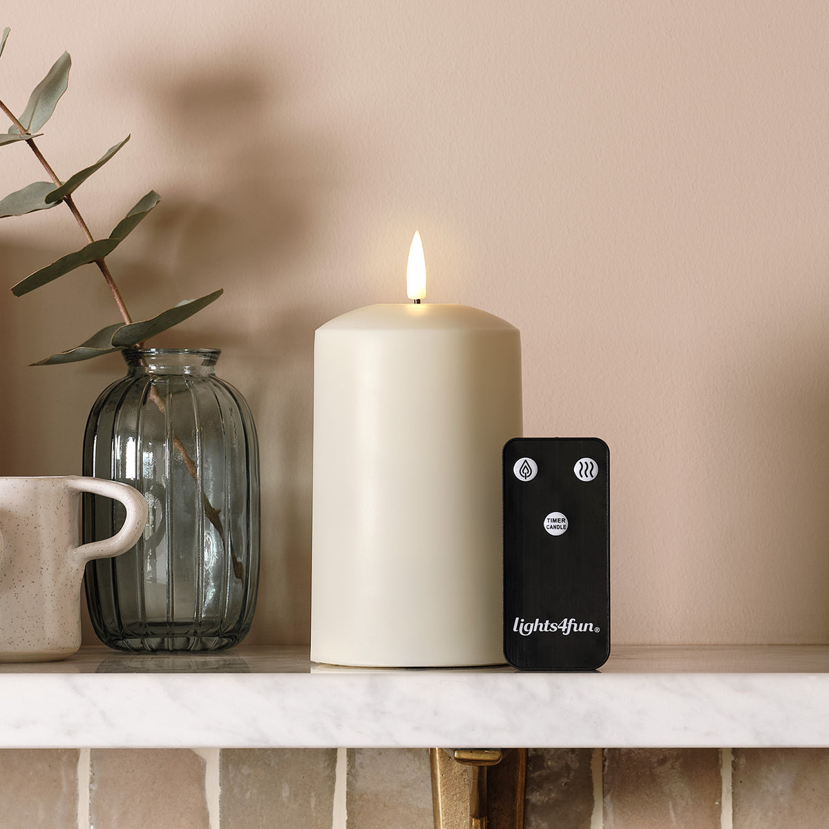 TruGlow AIR LED-Kerze mit Fernbedienung und Glasvase auf Marmorplatte vor beiger Wand