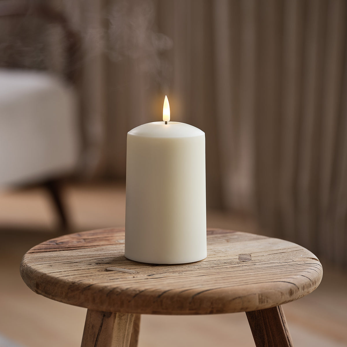 TruGlow AIR LED Kerze mit flackernder Flamme auf Holzschemel vor Vorhang im Hintergrund