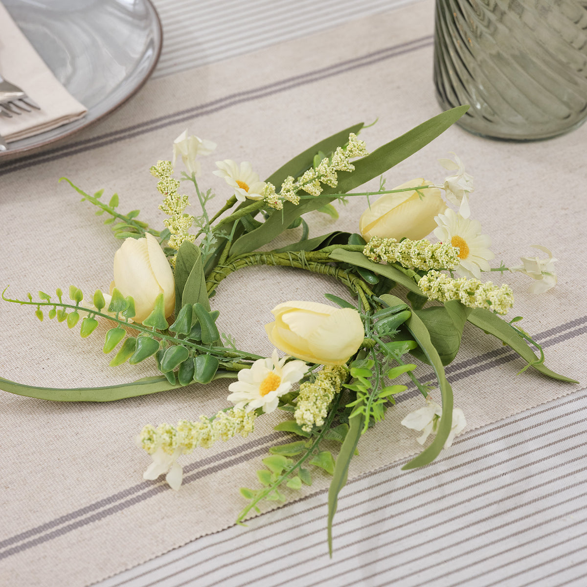 Frühlings-Kerzenring mit buttergelben Tulpen, Gänseblümchen und grünem Drahtring auf Stoffuntergrund