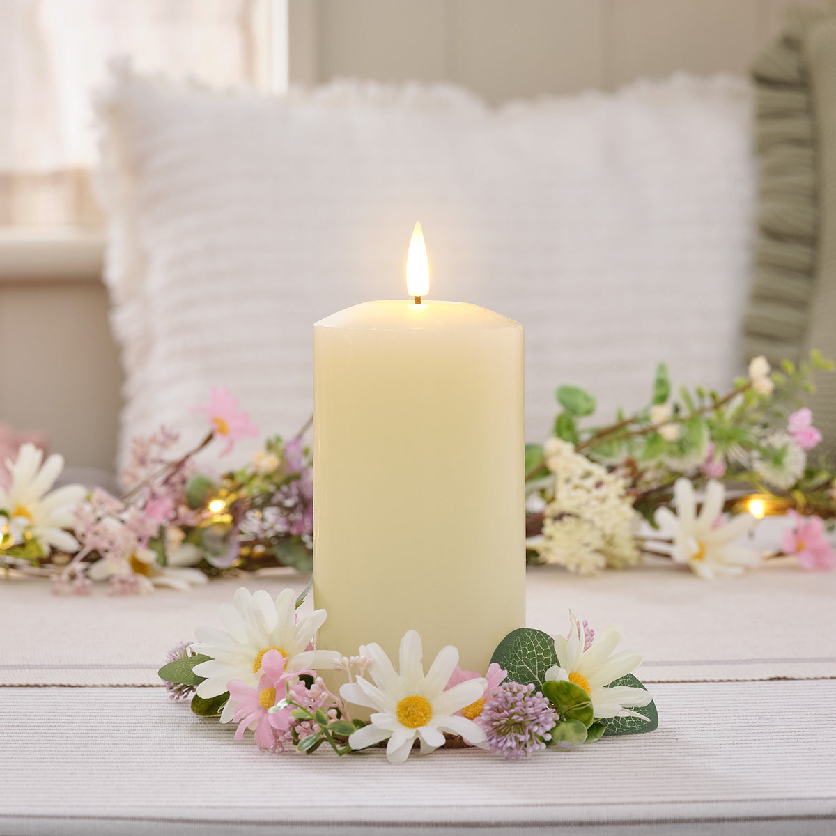 Elfenbeinfarbene LED-Stumpenkerze mit flackernder Flamme und pastellfarbenem Wildblumen-Kerzenring