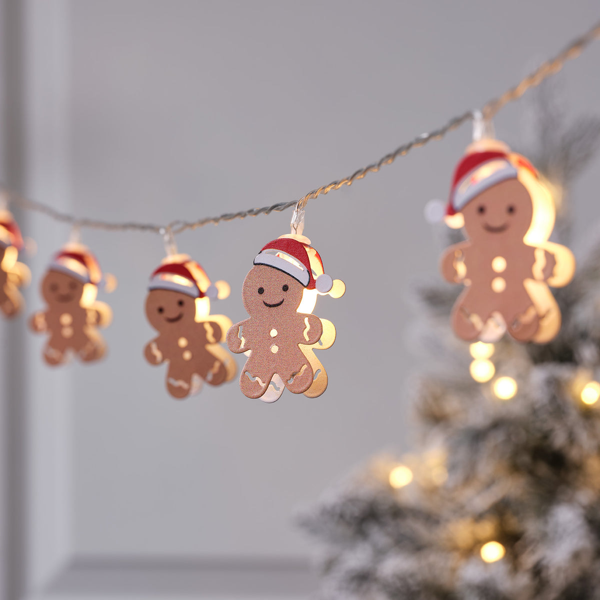 Nahaufnahme der leuchtenden Lebkuchenmännchen-Lichterkette mit Weihnachtsbaum im Hintergrund