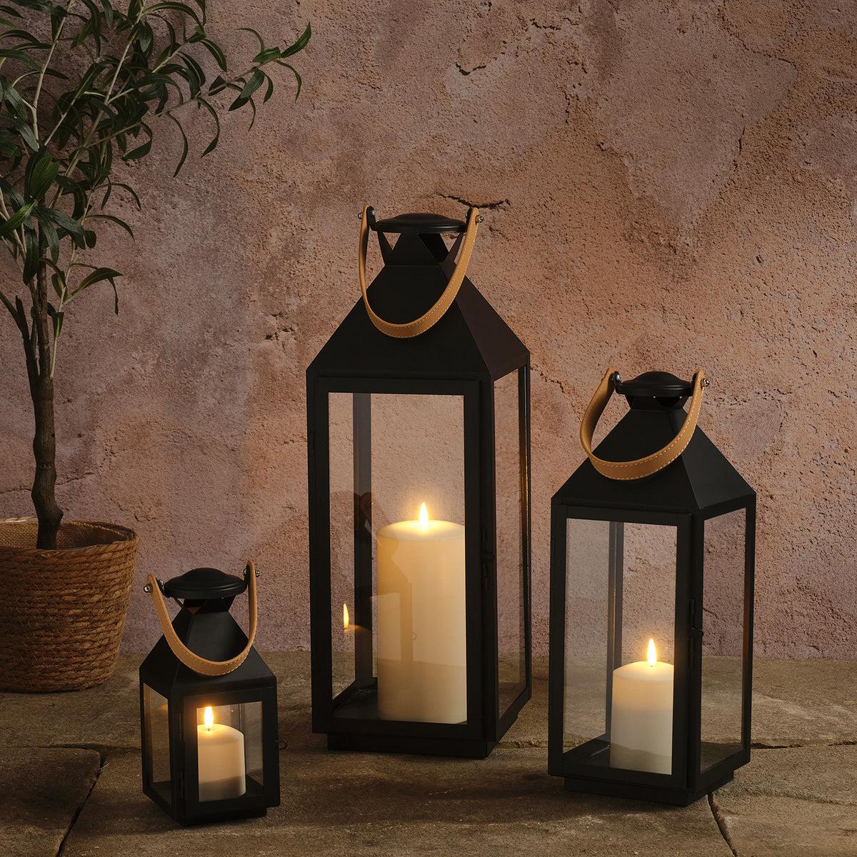 3er Set schwarze LED-Laternen mit Kunstledergriffen in Cognac und TruGlow Kerzen vor heller Wand
