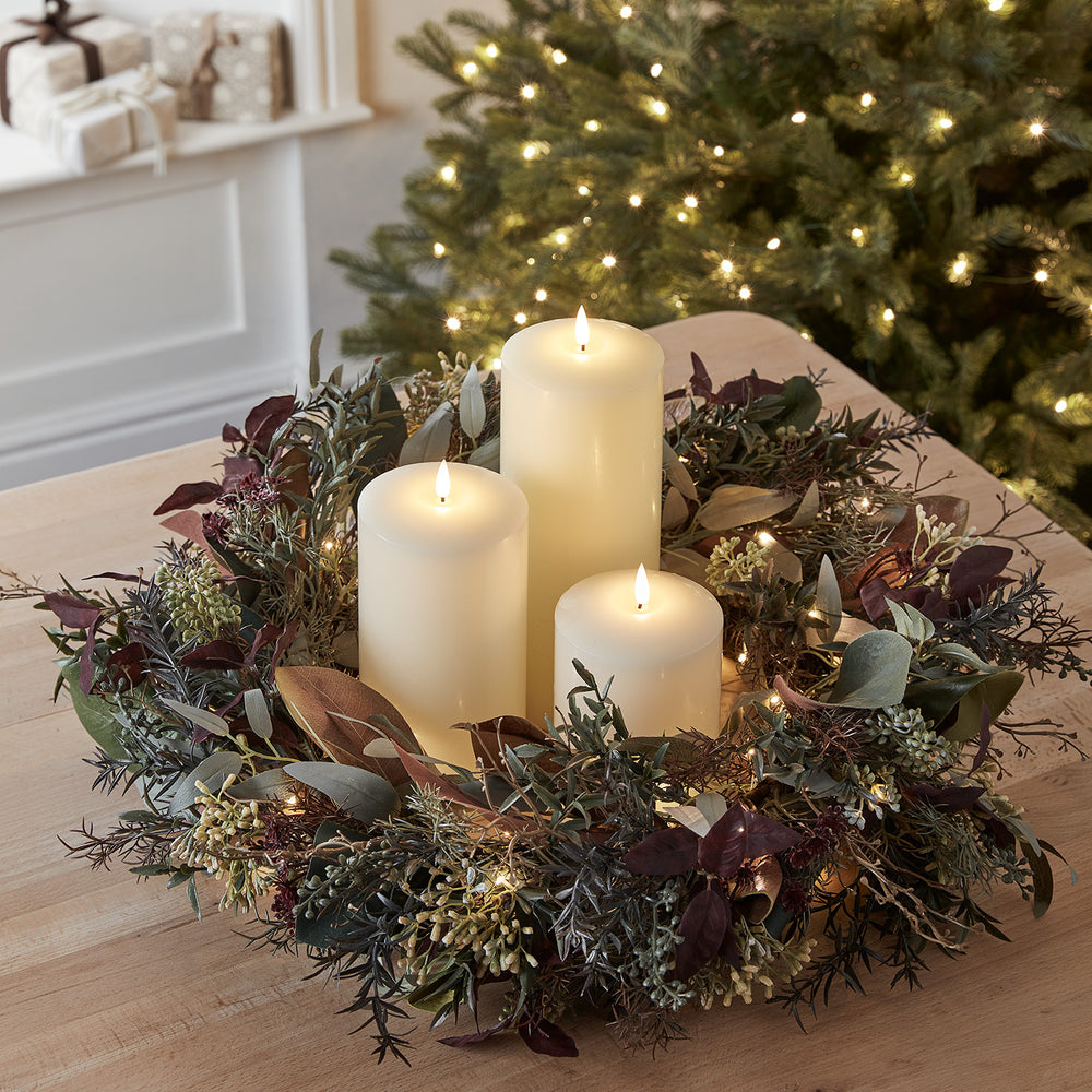 Herbstkranz mit beleuchteten Blättern und drei TruGlow LED-Kerzen vor Weihnachtsbaum mit Lichterkette