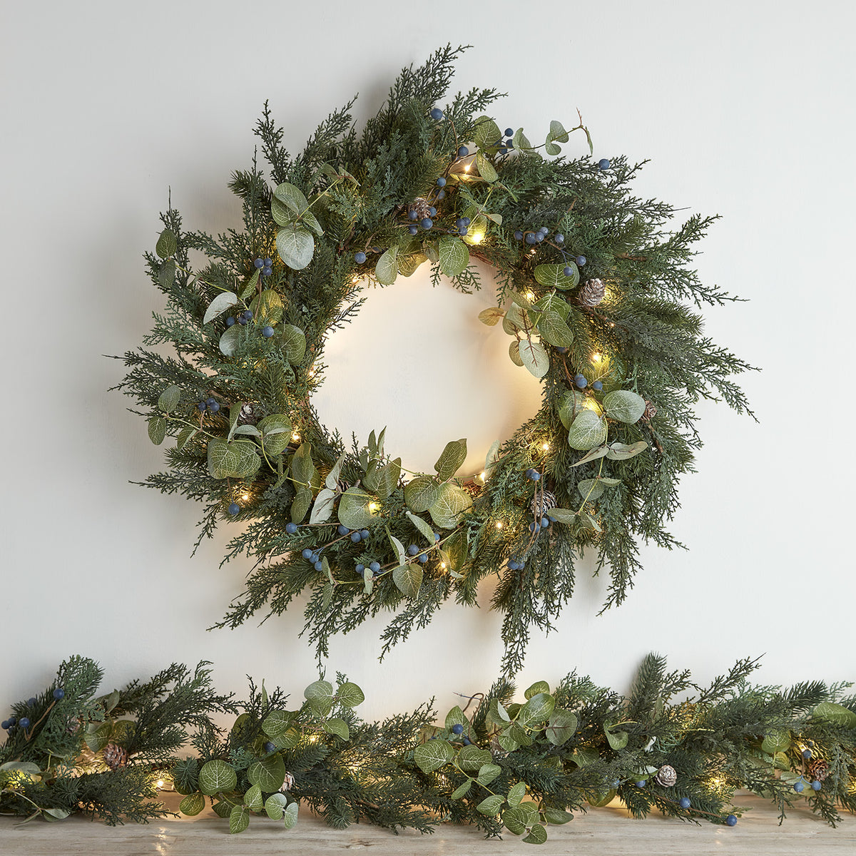 Weihnachtskranz mit grünen Tannenzweigen, Eukalyptusblättern, blauen Beeren, Tannenzapfen und warmweißen LED-Lichtern