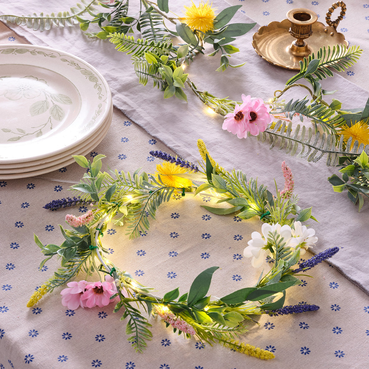 Frühlingskranz mit künstlichen Blumen und warmweißen LED-Lichtern auf gemustertem Tischläufer
