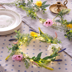 Frühlingskranz mit künstlichen Blumen und warmweißen LED-Lichtern auf gemustertem Tischläufer