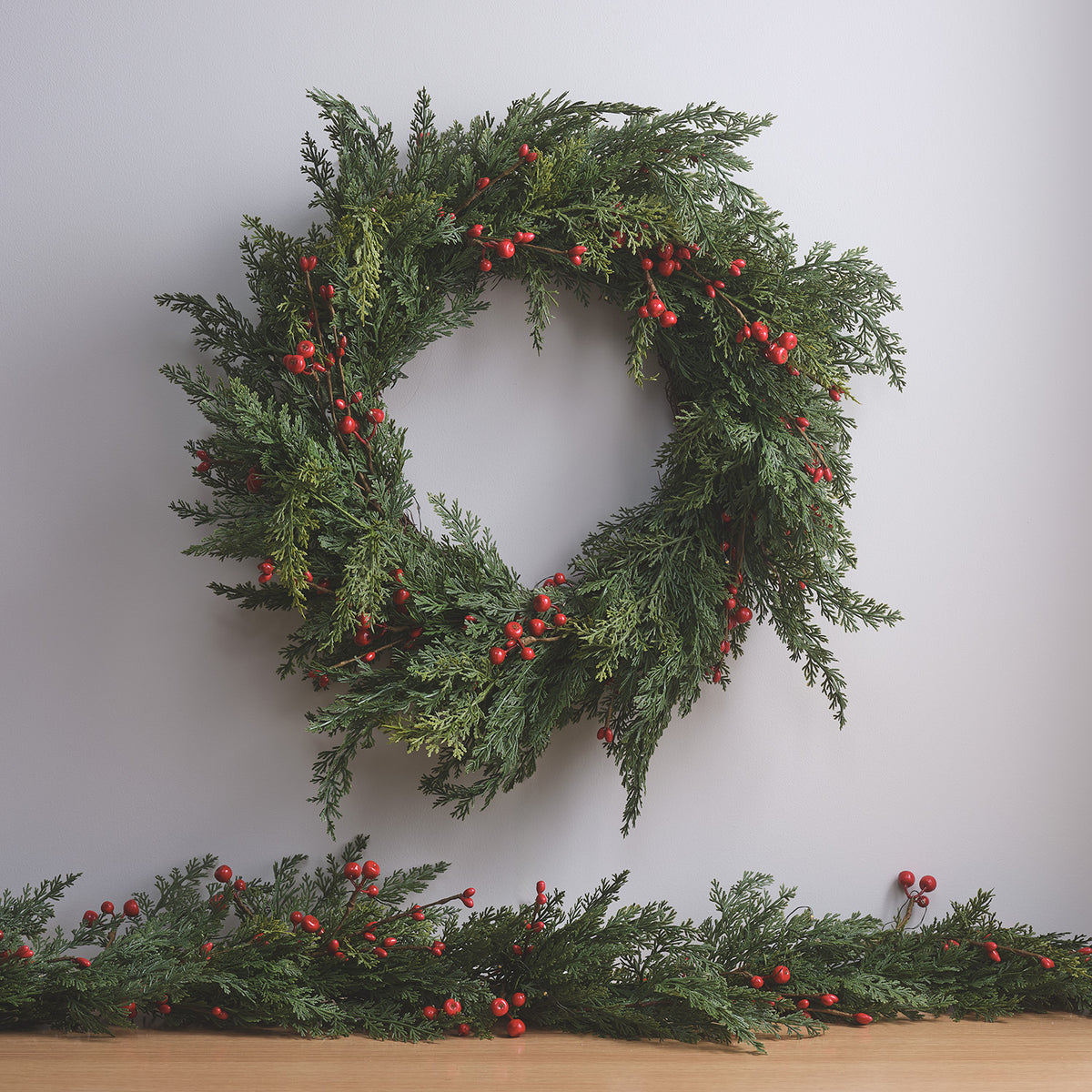 Weihnachtskranz mit roten Beeren und Tannengrün ohne Beleuchtung vor weißer Wand