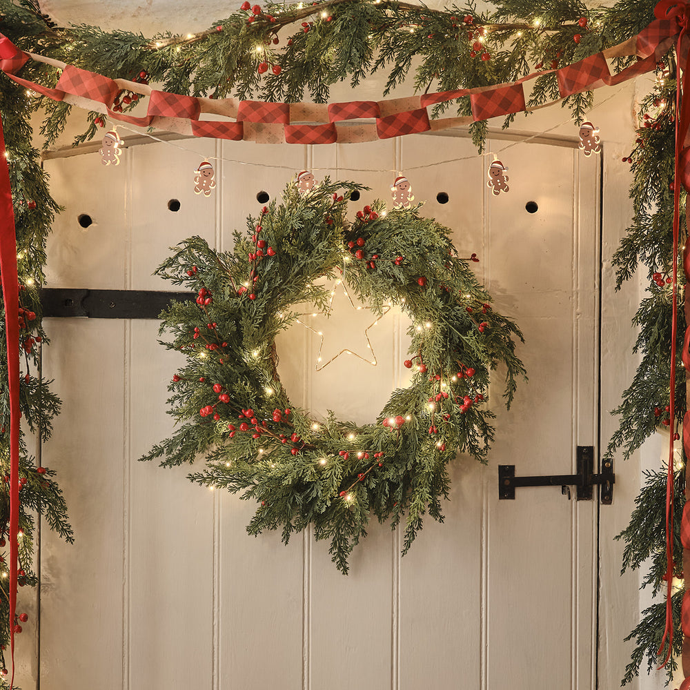 Beleuchteter Weihnachtskranz mit roten Beeren und Tannengrün an weißer Holztür dekoriert