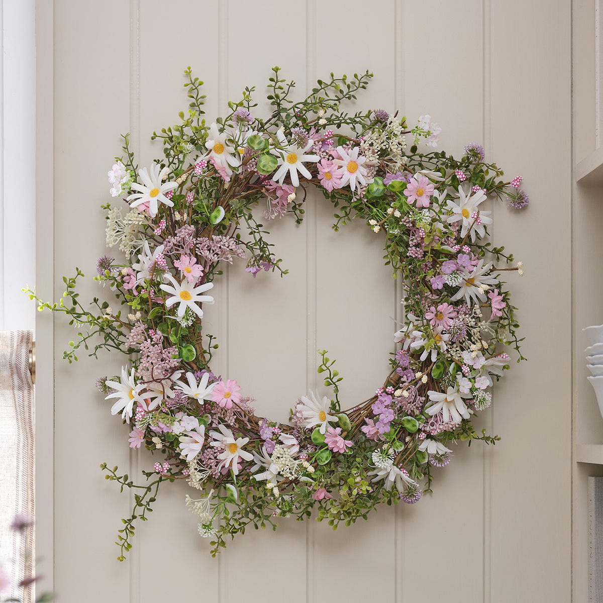LED-Blumenkranz mit Pastell-Margeriten und warmweißen LEDs an weißer Wand dekoriert