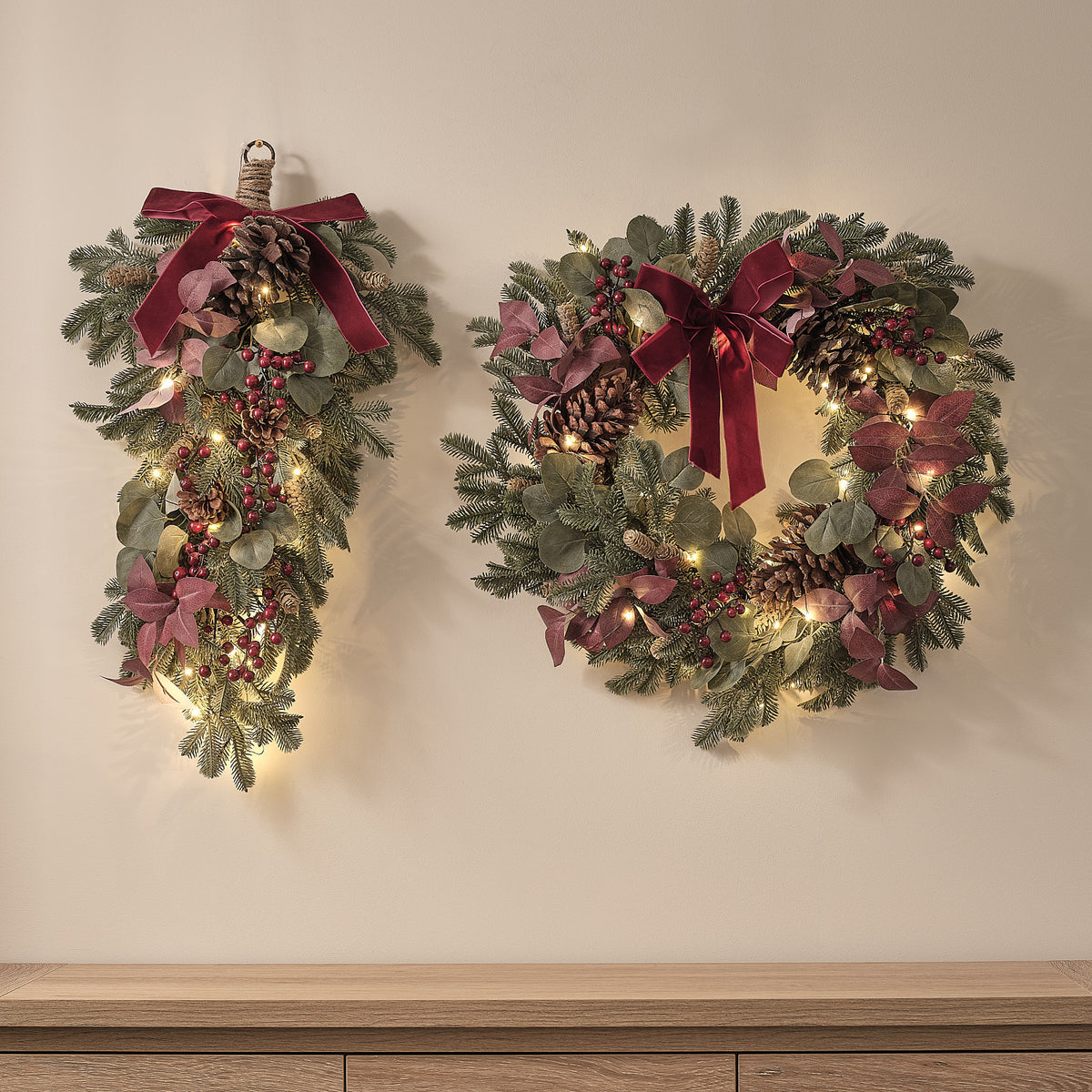 Beleuchteter Weihnachtskranz und Dekozweig mit roten Schleifen, Tannenzapfen und warmweißen LEDs an Wand