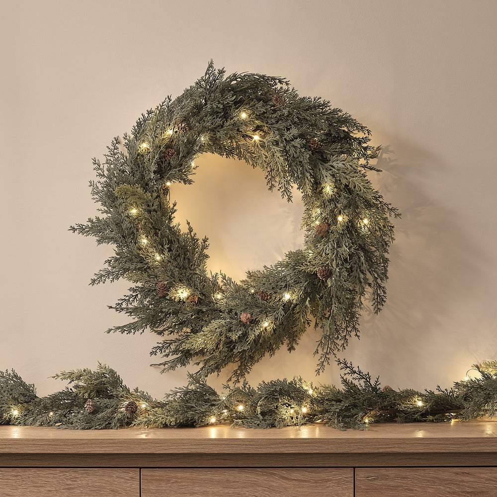 Beleuchteter Weihnachtskranz mit Tannenzapfen und warmweißen LEDs an Wand über Sideboard