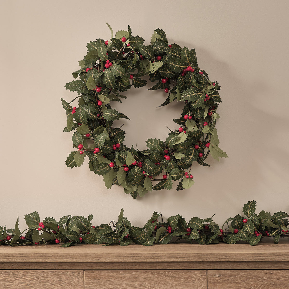 Weihnachtskranz mit Stechpalmenblättern und roten Beeren an Wand über Sideboard ohne Beleuchtung