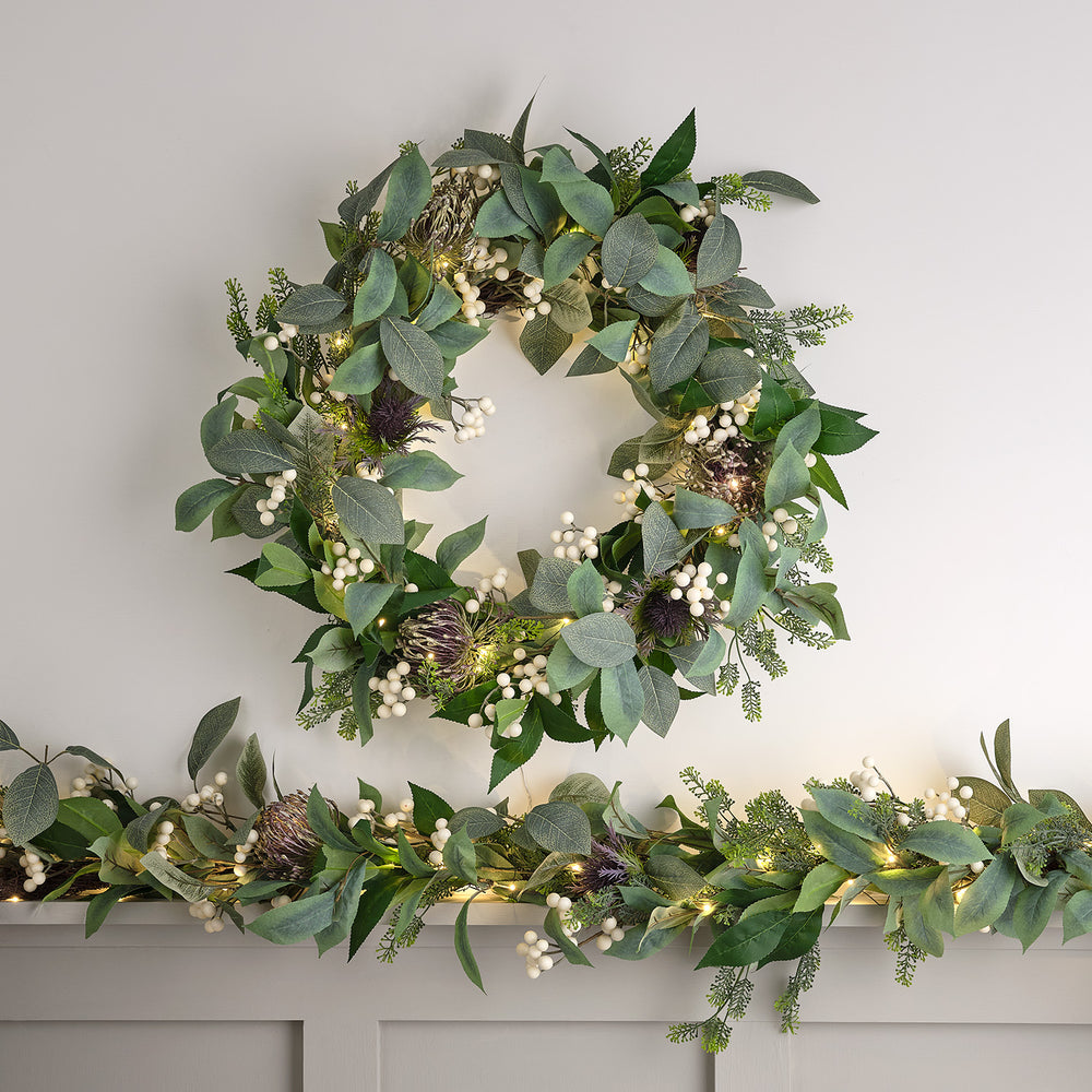 Beleuchteter Weihnachtskranz mit grünen Blättern und weißen Beeren auf hellem Hintergrund