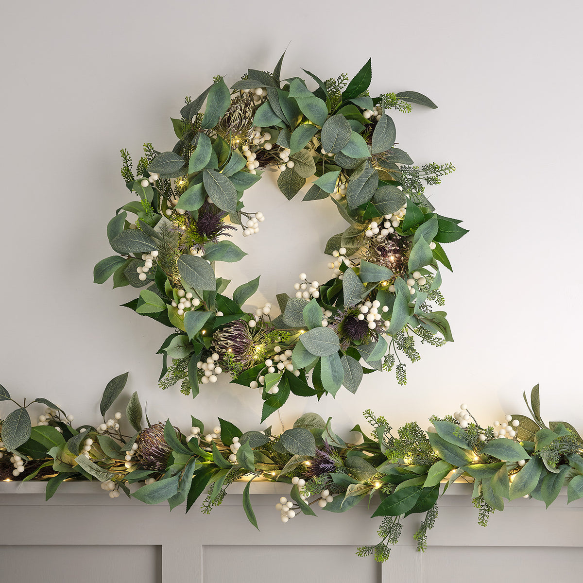 Beleuchteter Weihnachtskranz mit grünen Blättern und weißen Beeren auf hellem Hintergrund