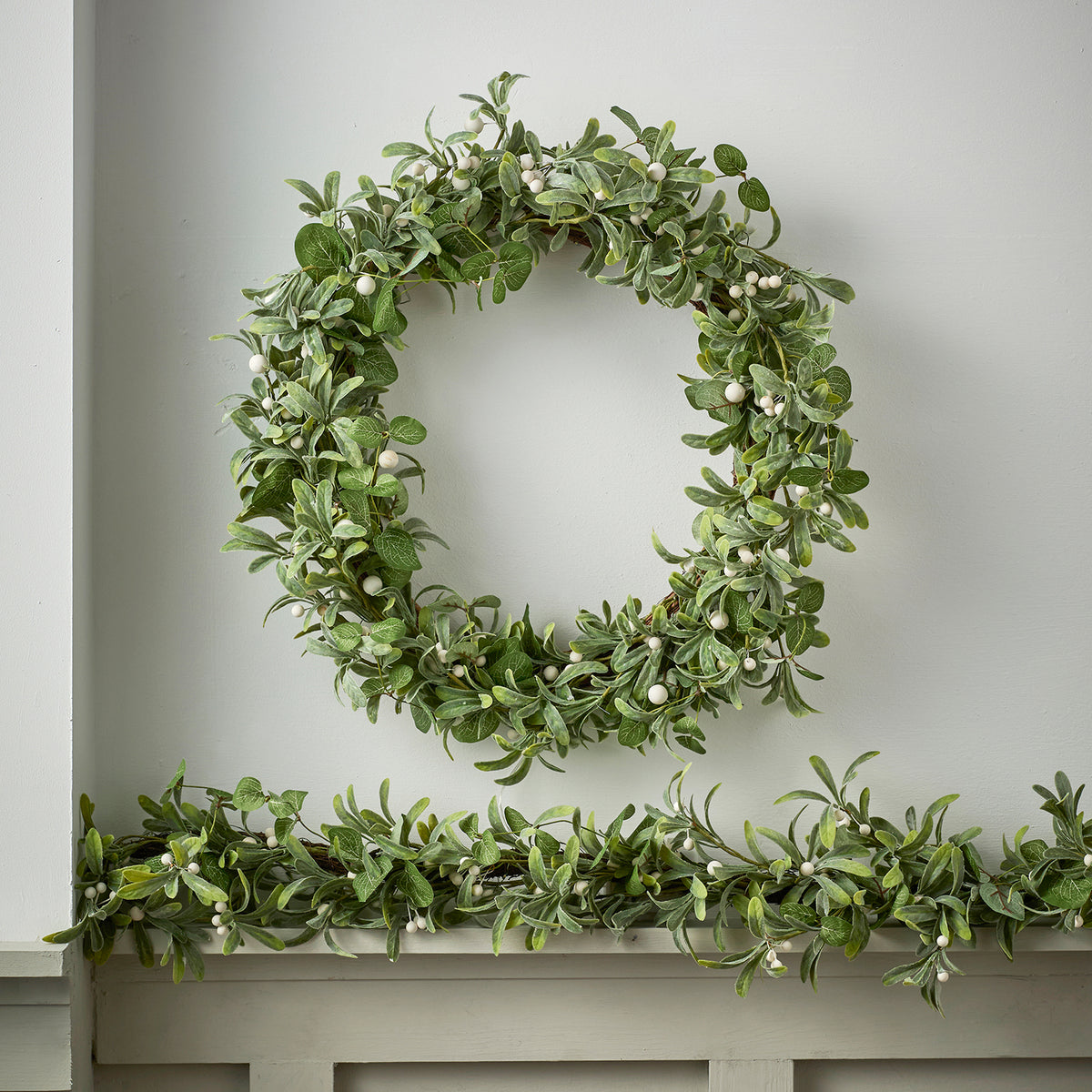 Weihnachtskranz mit grünen Blättern und weißen Beeren ohne Beleuchtung an weißer Wand