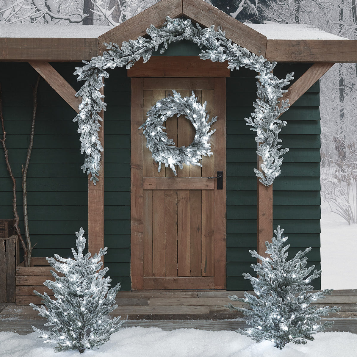Verschneiter Weihnachtskranz und Girlande mit zweifarbigen LEDs an Holztür und Eingang